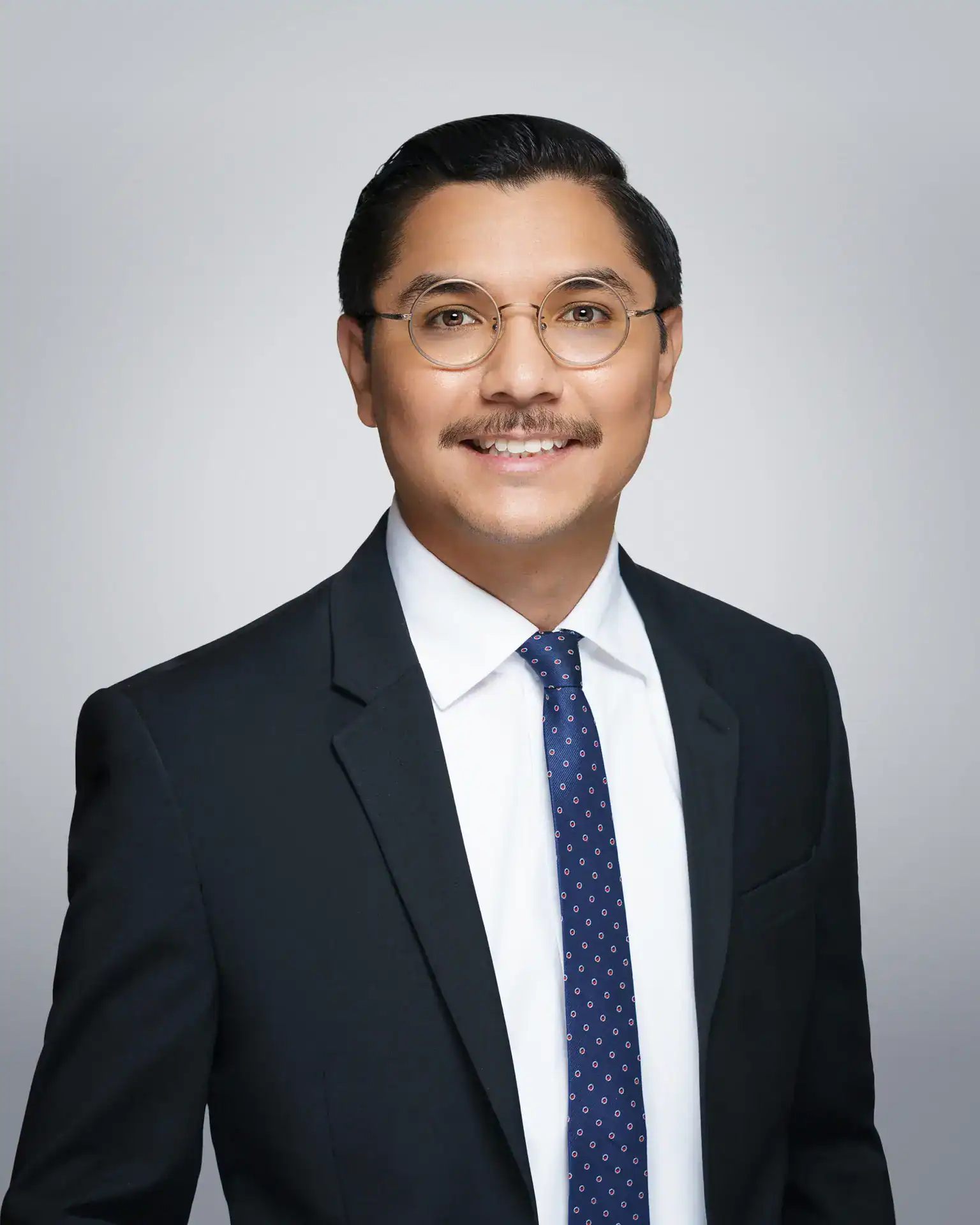 Portrait of Doll Amir Eley, a professional attorney in a dark suit and glasses.